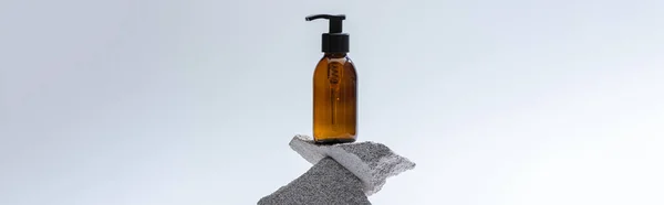 Dispensador garrafa cosmética em pedras no fundo branco com luz traseira, tiro panorâmico — Fotografia de Stock