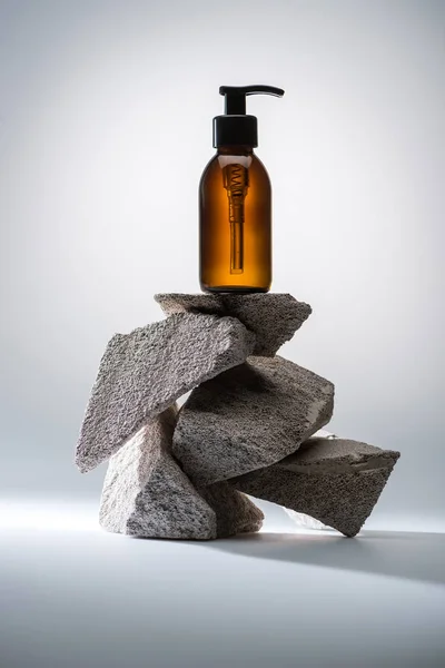 Dispensador botella cosmética sobre piedras sobre fondo blanco con luz de fondo - foto de stock