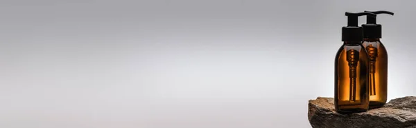 Dispenser cosmetic bottles on stone on white background with back light, panoramic shot — Stock Photo