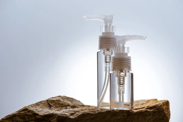 Dispensador de botellas de cosméticos en piedra sobre fondo blanco con luz de fondo - foto de stock