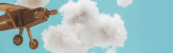 Wooden toy plane flying among white fluffy clouds made of cotton wool isolated on blue, panoramic shot — Stock Photo