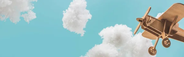 Wooden toy plane flying among white fluffy clouds made of cotton wool isolated on blue, panoramic shot — Stock Photo