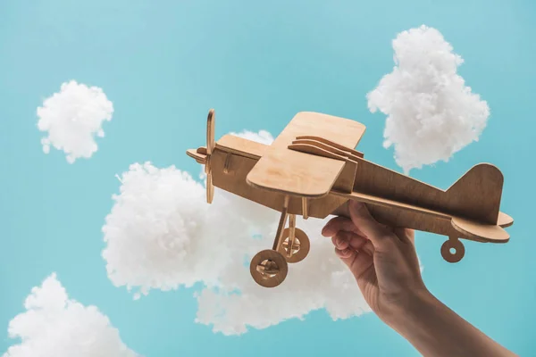 Avião de brinquedo de madeira voando entre nuvens brancas fofas feitas de lã de algodão isolado em azul — Fotografia de Stock