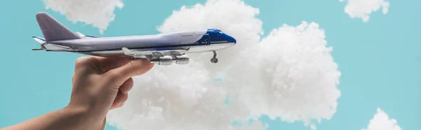 Abgeschnittene Ansicht einer Frau, die mit einem Spielzeugflugzeug spielt, inmitten weißer, flauschiger Wolken aus Watte isoliert auf blauem Grund, Panoramaaufnahme — Stockfoto