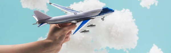 Cropped view of woman playing with toy plane among white fluffy clouds made of cotton wool isolated on blue, panoramic shot — Stock Photo