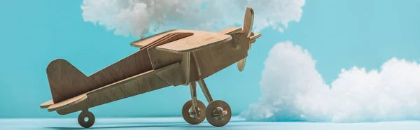 Avión de juguete de madera entre nubes esponjosas blancas hechas de algodón aislado en azul, tiro panorámico - foto de stock