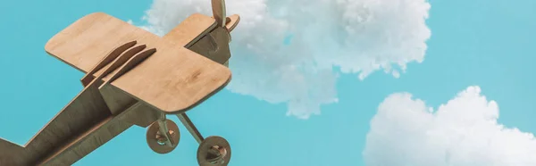 Avión de juguete de madera volando entre nubes esponjosas blancas hechas de algodón aislado en azul, plano panorámico - foto de stock