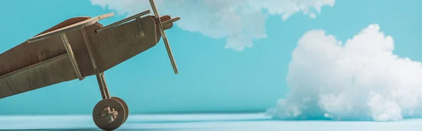 Avión de juguete de madera entre nubes esponjosas blancas hechas de algodón aislado en azul, tiro panorámico - foto de stock