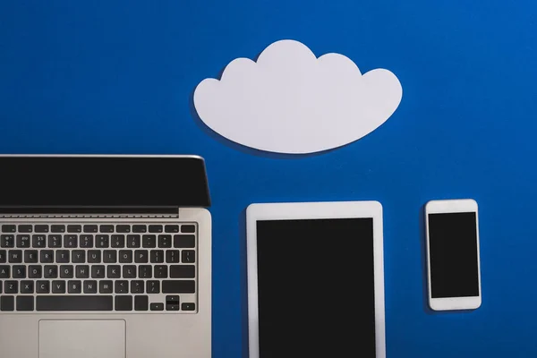Draufsicht auf leere weiße Papierwolke in der Nähe von Laptop, Smartphone und digitalem Tablet mit leerem Bildschirm isoliert auf blau — Stockfoto