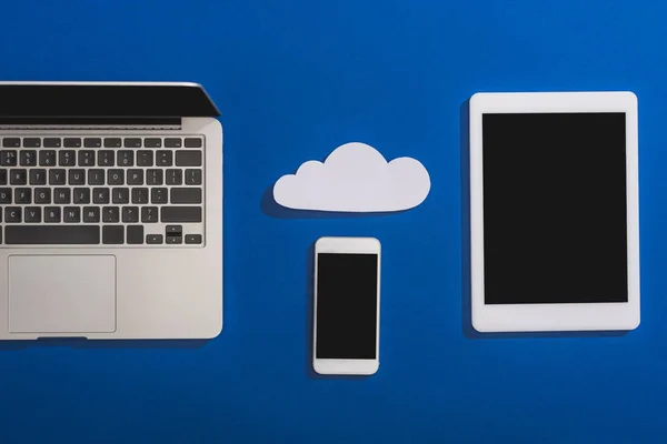 Top view of empty white paper cloud near laptop, smartphone and digital tablet with blank screen isolated on blue — Stock Photo