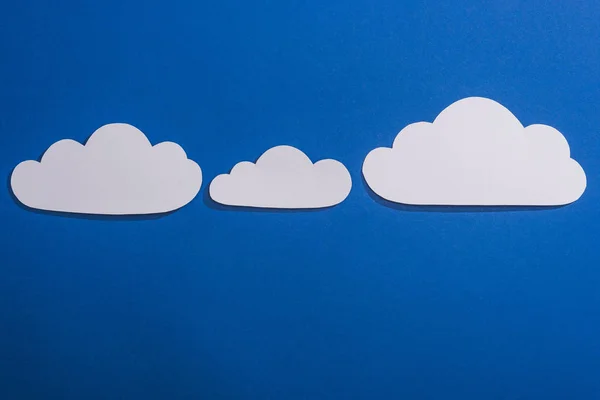 Vista superior del papel blanco cortado nubes sobre fondo azul - foto de stock