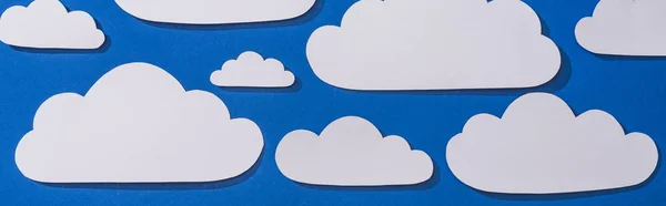 Vista superior del papel blanco cortado nubes sobre fondo azul, plano panorámico - foto de stock