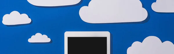 Top view of white paper cut clouds and digital tablet on blue background, panoramic shot — Stock Photo