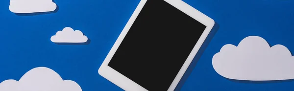 Vista superior del papel blanco cortado nubes y tableta digital sobre fondo azul, plano panorámico - foto de stock