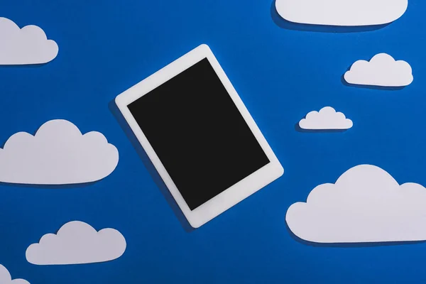 Top view of white paper cut clouds and digital tablet on blue background — Stock Photo