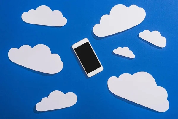 Top view of white paper cut clouds and smartphone on blue background — Stock Photo