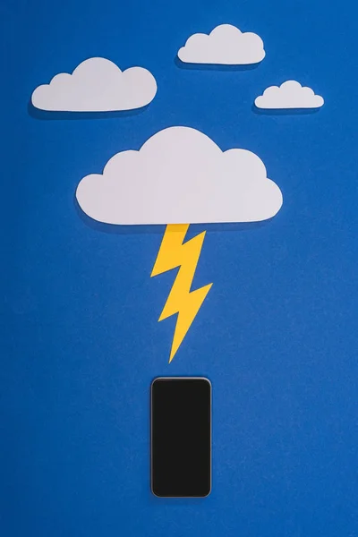 Draufsicht auf weiße Papier geschnittene Wolken mit Beleuchtung treffen Smartphone auf blauem Hintergrund — Stockfoto