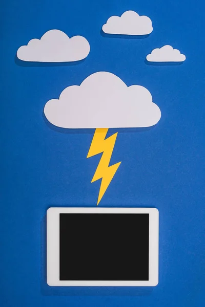 Vue du dessus des nuages coupés en papier blanc avec éclairage frappant tablette numérique sur fond bleu — Photo de stock