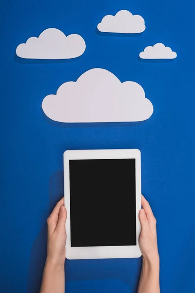 Abgeschnittene Ansicht einer Frau, die ein digitales Tablet in der Nähe von weißen Papierwolken auf blauem Hintergrund hält — Stockfoto