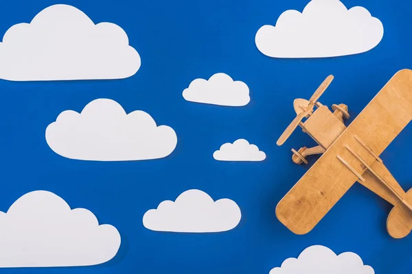 Vue du dessus de l'avion jouet en bois dans le ciel bleu avec du papier coupé nuages blancs — Photo de stock