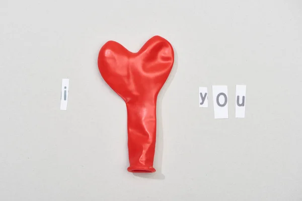 Vue du dessus de je t'aime lettrage avec ballon en forme de coeur rouge sur fond gris — Photo de stock