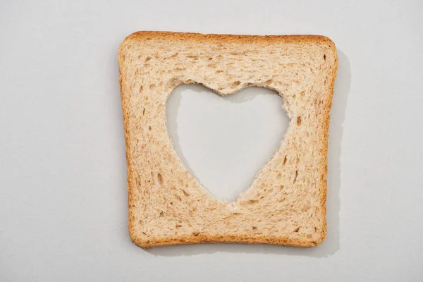 Top view of bread slice with carved heart shape on grey background — Stock Photo