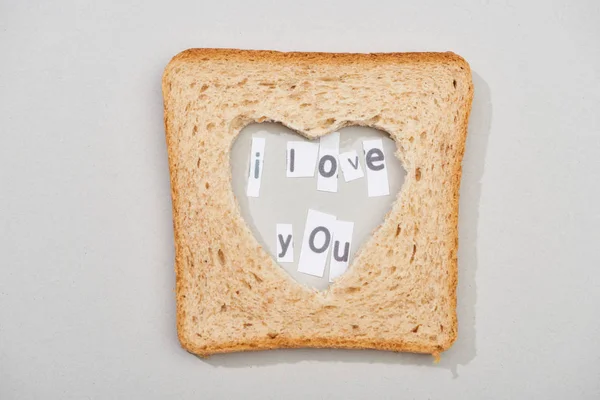 Vista superior de rebanada de pan con forma de corazón tallado y te amo letras sobre fondo gris - foto de stock