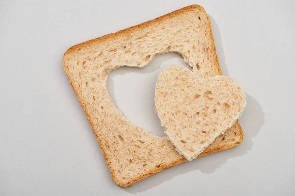 Вид сверху куска хлеба с вырезанным сердцем на сером фоне — стоковое фото