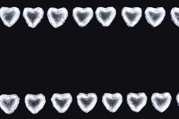 Top view of lines from heart shaped sweets in foil isolated on black — Stock Photo