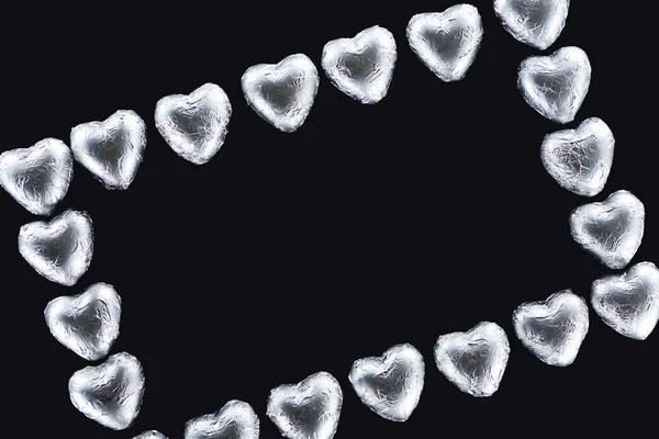 Top view of frame with heart shaped candies in foil isolated on black with copy space — Stock Photo