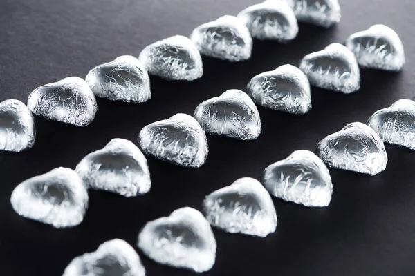 Heart shaped candies in foil on black background — Stock Photo