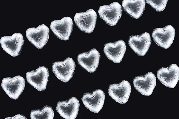 Top view of lines from heart shaped sweets in foil isolated on black — Stock Photo