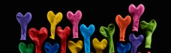 Top view of colorful rubber balloons in heart shape isolated on black, panoramic shot — Stock Photo