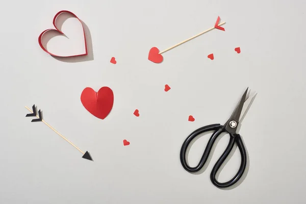 Vista superior de papeles en forma de corazón con flechas y tijeras sobre fondo gris - foto de stock