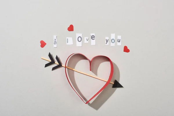 Vista superior de corazones de papel con flecha y te amo con letras sobre fondo gris - foto de stock