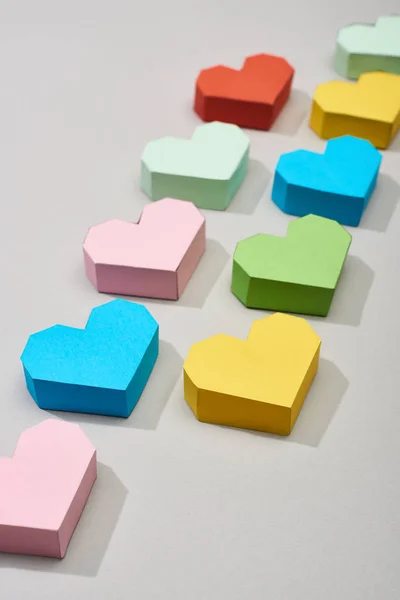 Linhas com papéis coloridos em forma de coração sobre fundo cinza — Fotografia de Stock