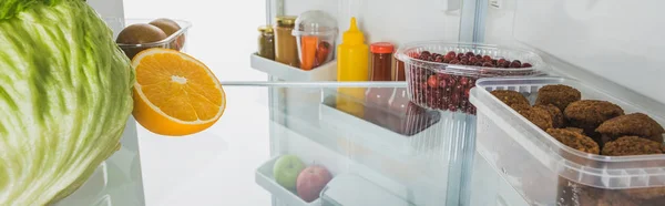 Свежие фрукты, котлеты и соусы в холодильнике с открытой дверью, изолированной на белом, панорамный снимок — стоковое фото