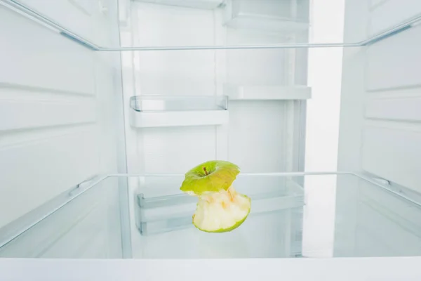 Gnawed green apple on shelf of refrigerator with open door isolated on white — Stock Photo