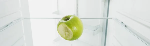Tiro panorâmico de maçã verde mordida na prateleira do refrigerador com porta aberta isolada em branco — Fotografia de Stock