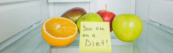 Panoramic shot of fresh fruits on fridge shelf with you are on a diet lettering on card — Stock Photo
