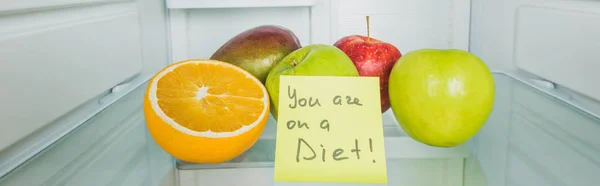 El tiro panorámico de frutas frescas en el estante de la nevera con usted está en una letra de la dieta en tarjeta - foto de stock