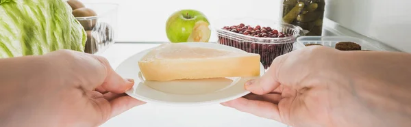 Abgeschnittene Ansicht einer Frau, die Käse aus dem Kühlschrank nimmt, mit Lebensmitteln isoliert auf weißer, panoramischer Aufnahme — Stockfoto