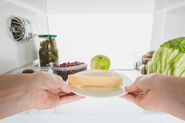 Vista recortada de la mujer tomando queso de la nevera con frutas y encurtidos aislados en blanco - foto de stock