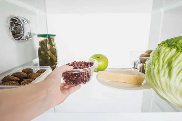 Vista recortada de la mujer tomando grosella fresca de la nevera con alimentos aislados en blanco - foto de stock