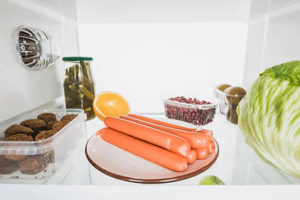 Sausages, fresh fruits and cabbage on fridge shelf isolated on white — Stock Photo