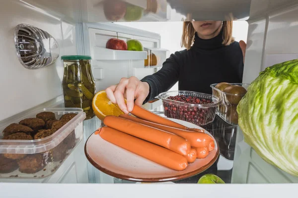 Vista cortada da mulher tomando salsicha da geladeira com alimentos isolados em branco — Fotografia de Stock