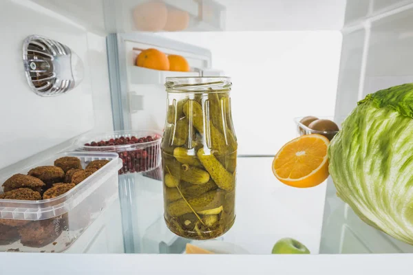 Tarro de encurtidos con col, frutas y chuletas en nevera con puerta abierta aislada en blanco - foto de stock