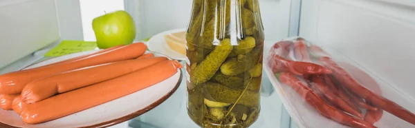 Photo panoramique de saucisses avec cornichons et piments au réfrigérateur avec porte ouverte isolée sur blanc — Photo de stock