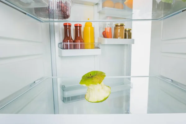 Selective focus of bitten apple with sauces on open fridge door isolated on white — Stock Photo