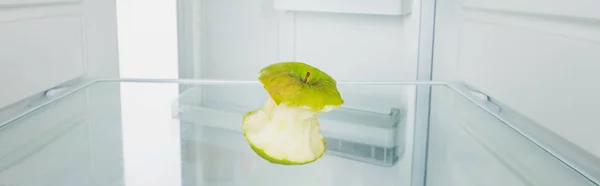 Foto panorámica de manzana verde roída en nevera con puerta abierta aislada en blanco - foto de stock